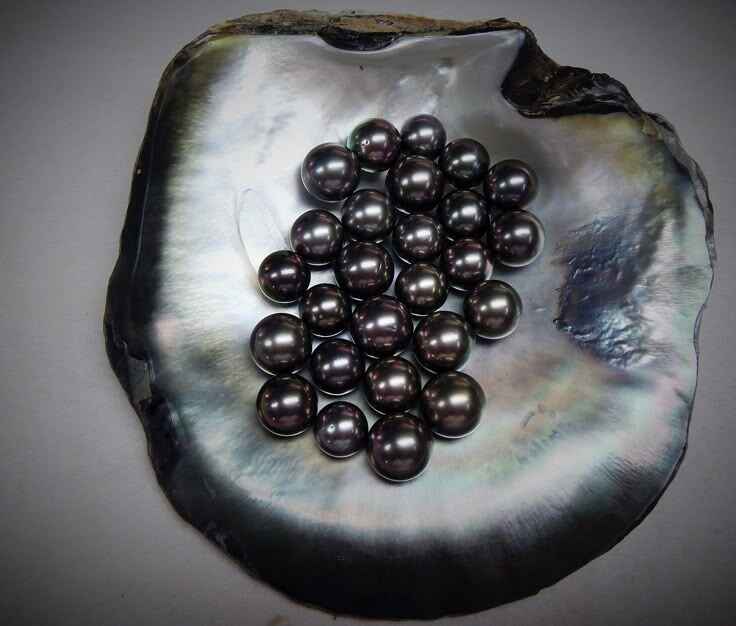 Glossy black Tahitian pearls with iridescent tones on white silk fabric – showcasing luxury and natural rarity of high-value pearls.