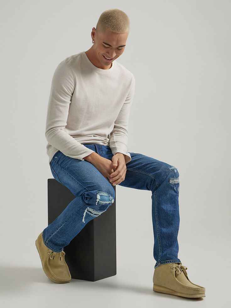 Man sitting wearing ripped slim fit jeans and beige casual shoes.