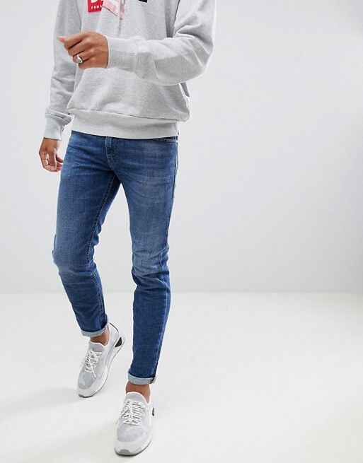 Slim fit blue jeans paired with casual sneakers and grey hoodie for men.