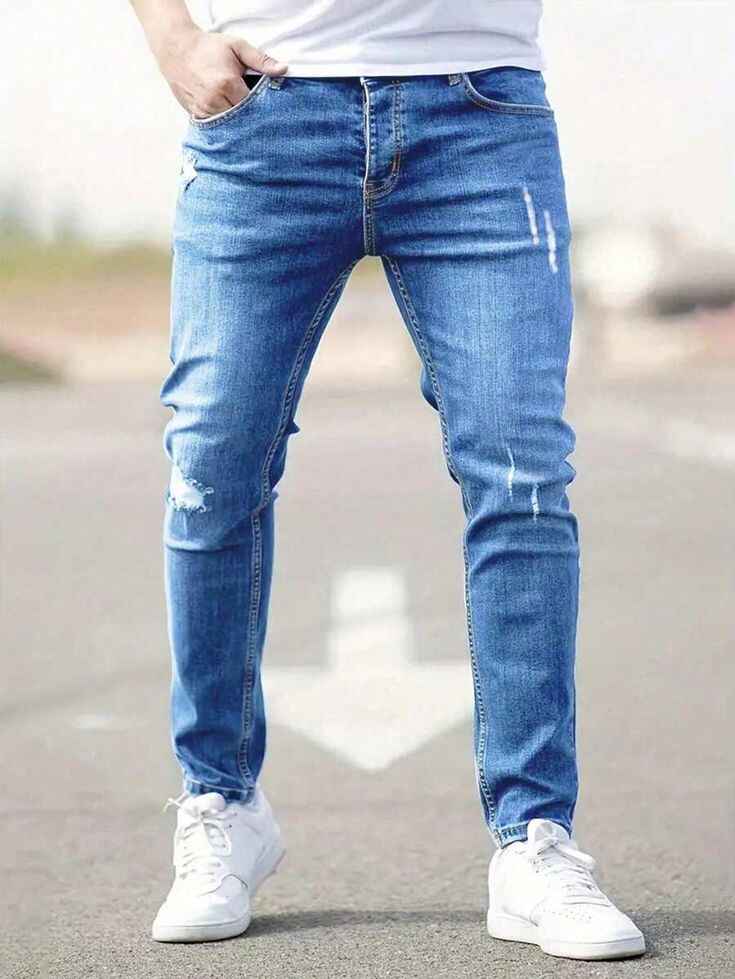 Front view of distressed slim fit blue jeans with white sneakers.
