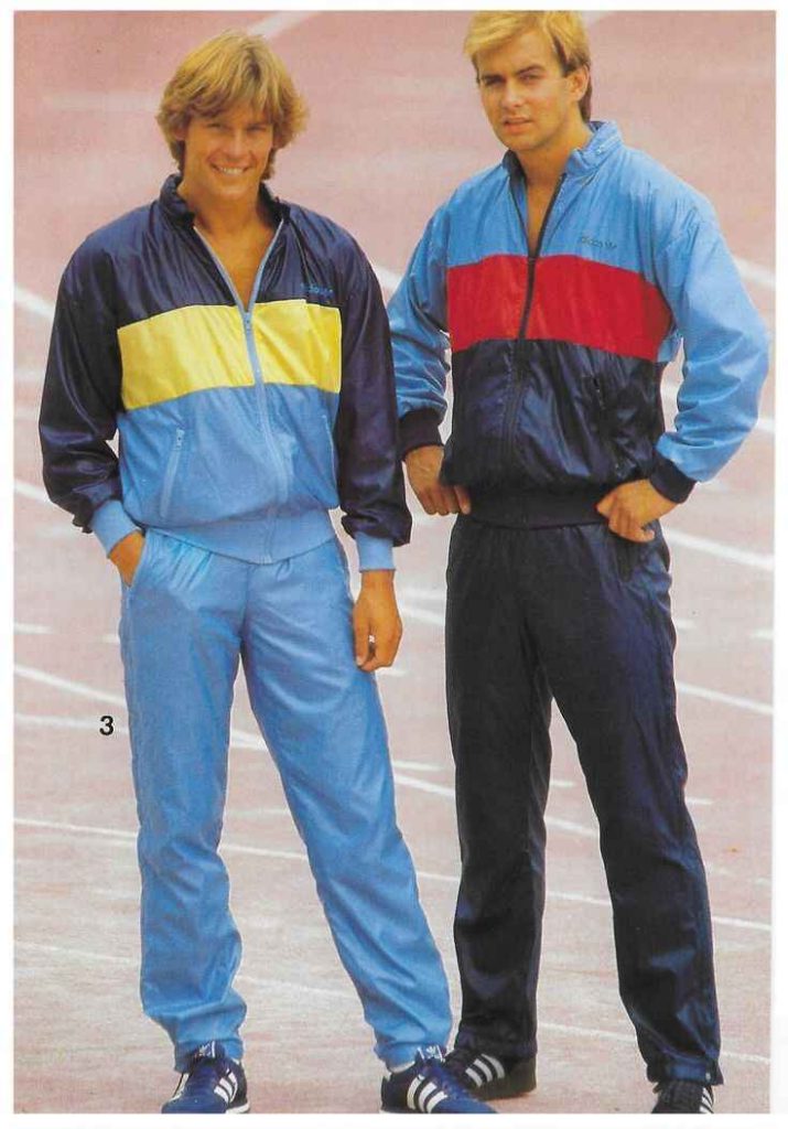 Two men in matching retro track suits with vibrant colors, Adidas shoes, and sporty 80s style.
