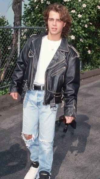 Man wearing a black leather jacket, ripped jeans, and white sneakers, showcasing a vintage 80s style.